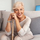 Woman in beige clothes on beige couch leaning on cane
