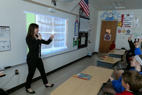 A member of the dental team talking to a group of school-aged kids about oral hygiene