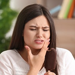 Woman sitting on couch holding her cheek in pain