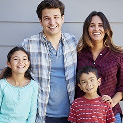 Family of four smiling in front of white wall