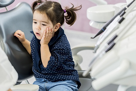 Little girl holding cheek in pain after primary tooth trauama