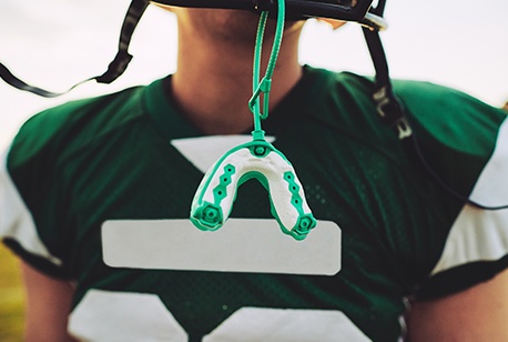 Teen boy with green athletic mouthguard hanging from football helmet