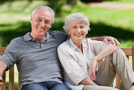 Smiling older man and woman with dentures on park bench