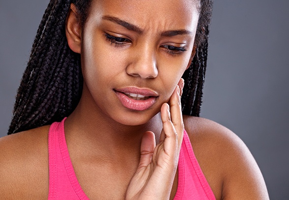 Young woman with braids and a toothache touching her cheek