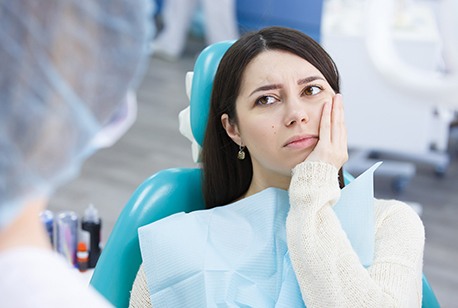 Frowning female patient holding her cheek looking at her dentist