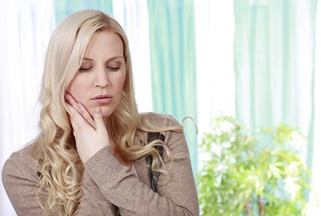 Young woman holding her cheek in pain while at home