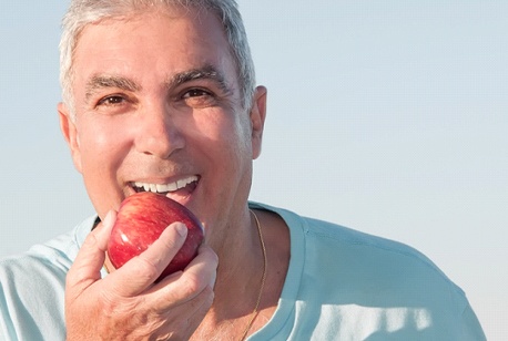 Older man biting an apple after full mouth reconstruction.