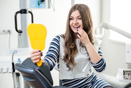 Woman in dental chair looking at her smile in a mirror.