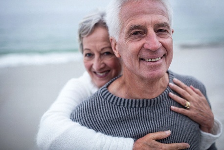 Older couple with implant dentures in Loveland smiling on beach