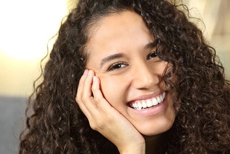A young woman with dark curly hair smiling about ways to protect her teeth from a dental emergency