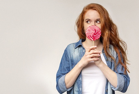 A young female with red hair holding a large lollipop in front of her face