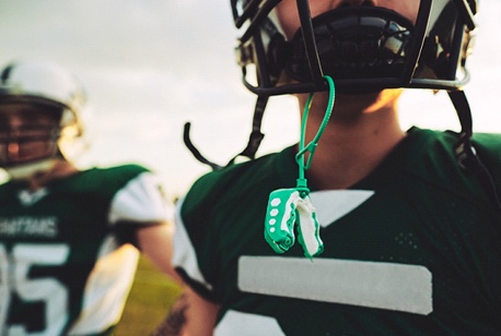 Two male football players, one with a green mouthguard hanging off his helmet