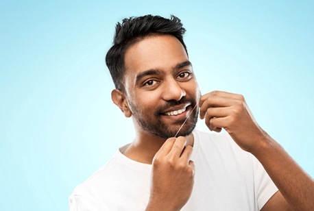 A young male holding dental floss in his hands and smiling