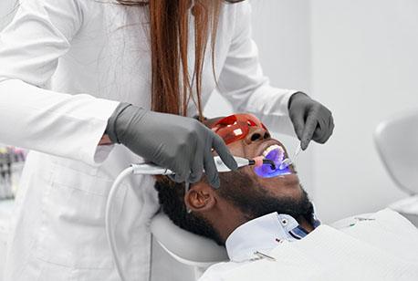 A dentist applying cosmetic dental bonding to a male patient’s smile