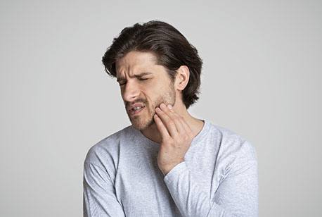 A young man holding his jaw and cringing in pain