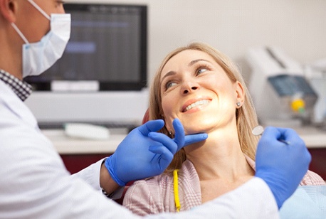 A middle-aged woman smiling at her dentist while he examines her teeth and gums during a regular checkup and cleaning
