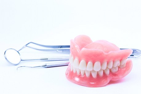 A set of full dentures sitting on a table next to multiple dental instruments