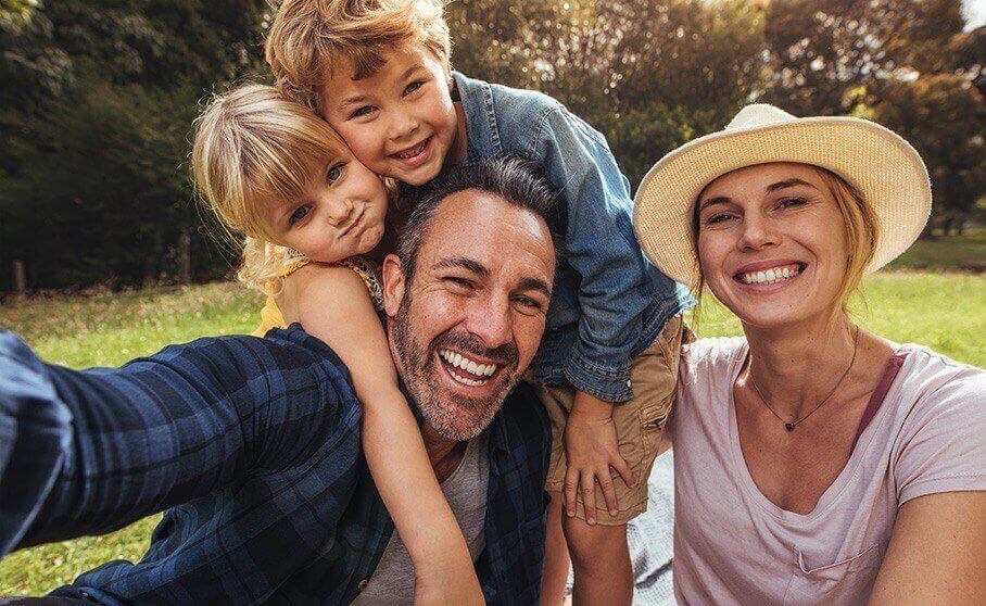 Mother father and two children smiling while sitting in grass outdoors