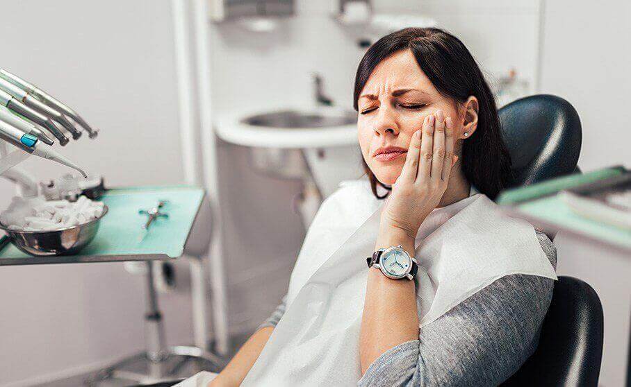 Woman in dental chair holding her cheek in pain