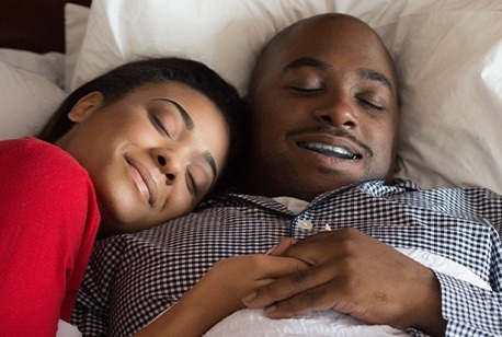 Man with sleep apnea oral appliance and woman sleeping in bed