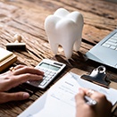 Hands on a desk with calculator, fake tooth, and invoice