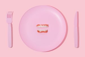 Set of dentures on a pink plastic plate on a pink background with pink cutlery