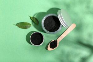 Bird's eye view of containers and spoon full of activated charcoal on green surface
